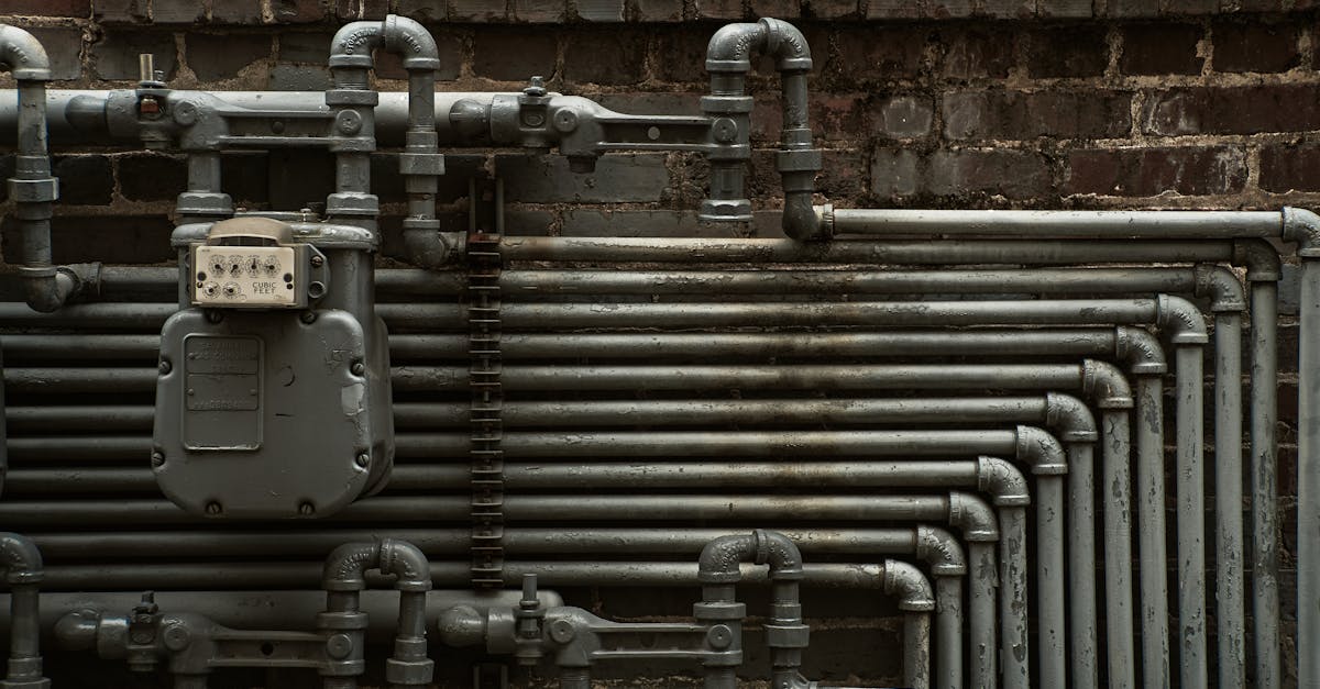 Detailed view of industrial steel pipes and a gas meter on a brick wall.